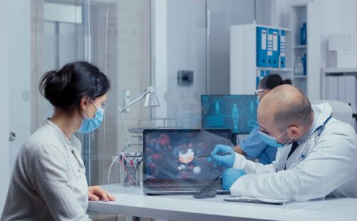 Doctor showing patient a coronavirus cell representation on a laptop, consultation during global health crisis. Medical consultation in protective equipment concept shot of sars-cov-2 global health pandemic crisis